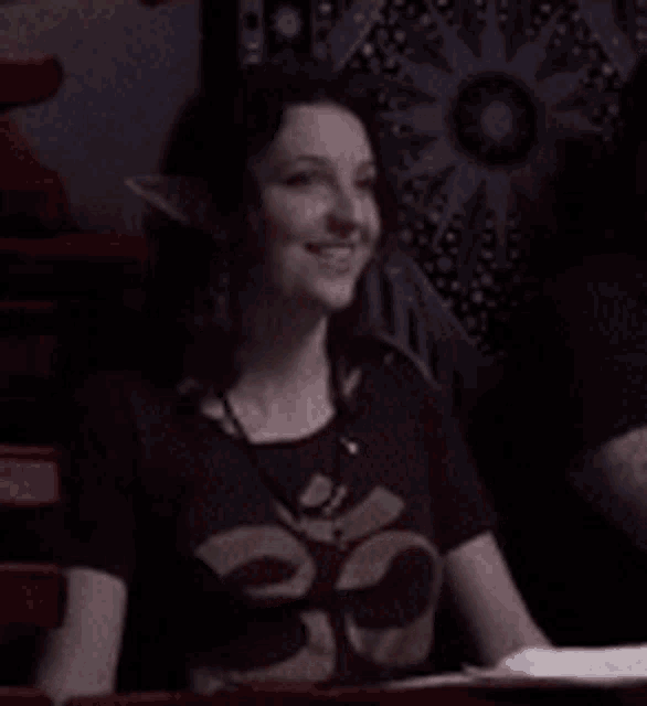 a woman is sitting at a table in a dark room wearing a t-shirt with a skull on it .