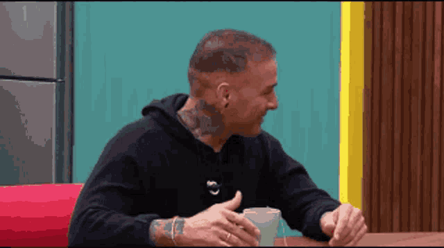 a man with a tattoo on his neck is sitting at a table with a glass of water