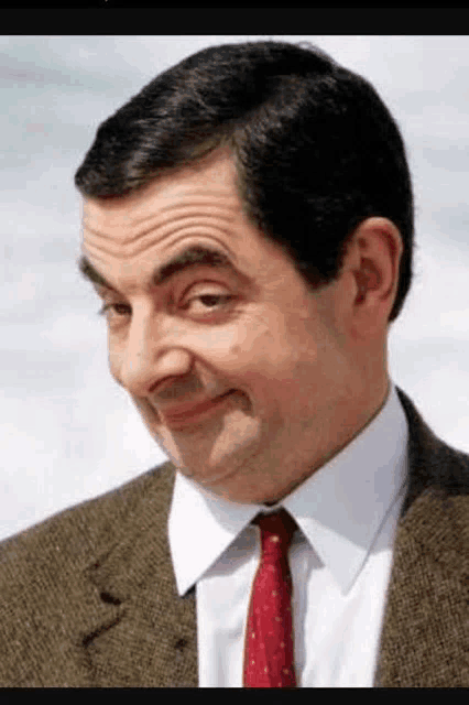 mr bean is wearing a suit and tie and making a face .