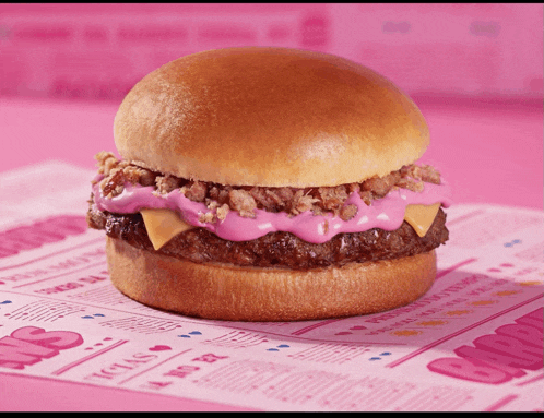 a hamburger with pink icing on top of it sits on a pink paper