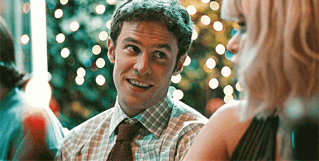 a man in a plaid shirt and tie is talking to a woman in a black dress .