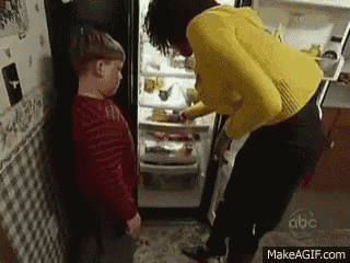 a woman in a yellow sweater is standing next to a boy in a red shirt in front of a refrigerator door ..