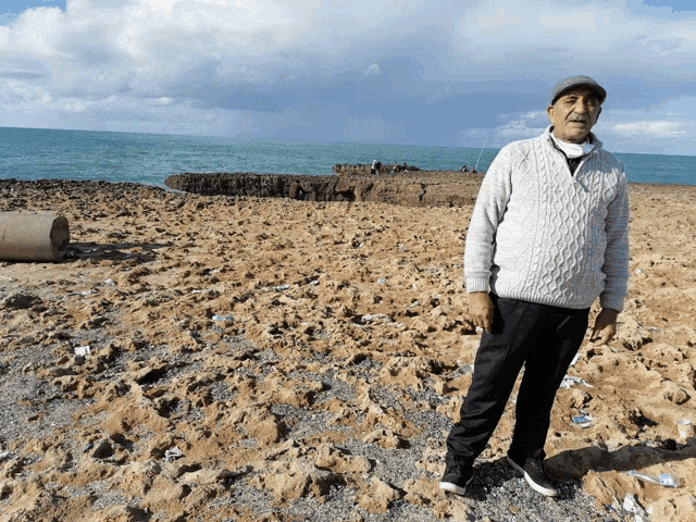 a man in a white sweater stands on a rocky beach near the ocean