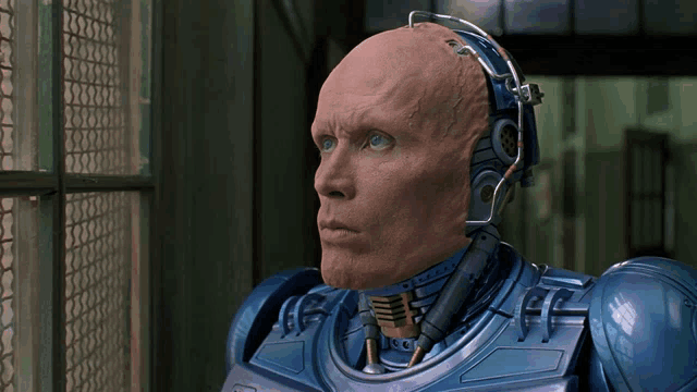 a robot with a bald head and headphones on looks out a window