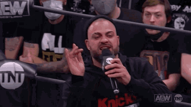 a man is talking into a microphone while sitting in a crowd of people .