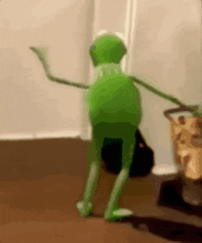 a green kermit the frog is dancing on a wooden floor in a room .