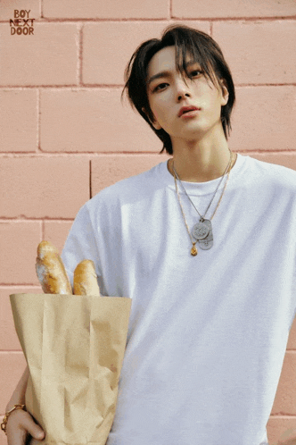 a young man in a white shirt is holding a bag of bread with boy next door written on the bottom