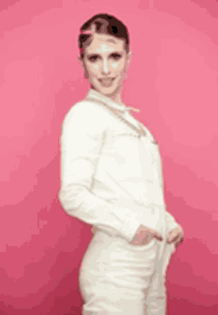 a woman in a white suit is standing in front of a pink background