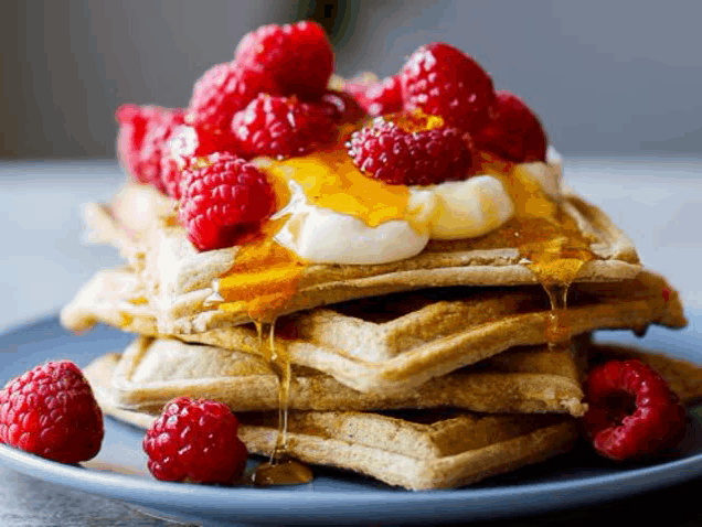 a stack of waffles with raspberries , syrup and whipped cream on a plate .