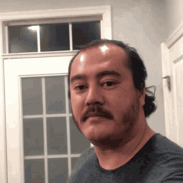 a man with a mustache is taking a selfie in front of a window