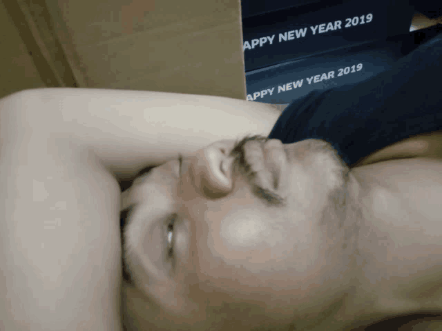 a man with a beard is laying down in front of a stack of boxes that say happy new year 2019