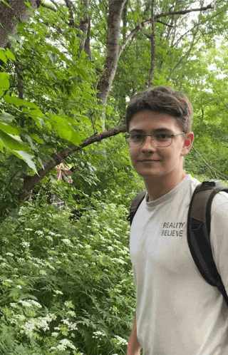 a young man wearing glasses and a reality believe shirt