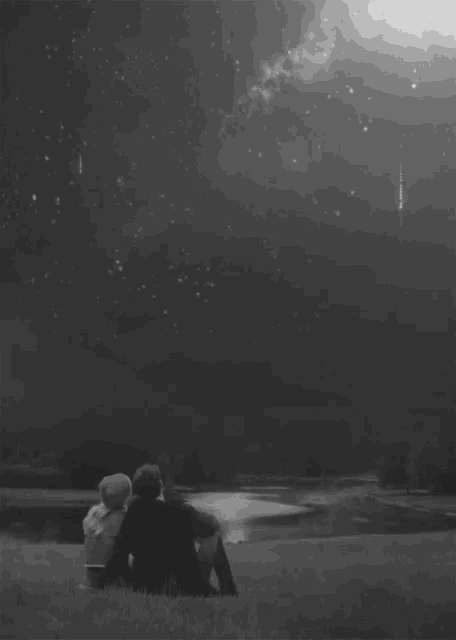 a black and white photo of a couple sitting under a starry night sky