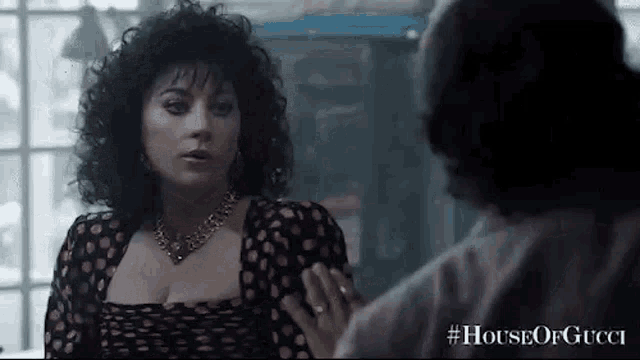 a woman in a polka dot dress is talking to a man in a house of gucci .