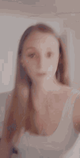 a blurry picture of a woman in a white tank top with long hair .