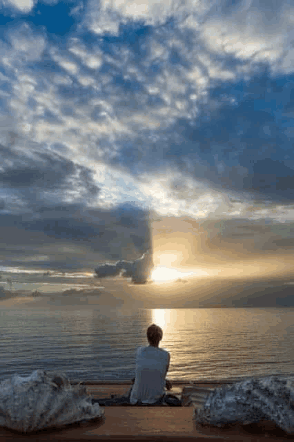 a person is sitting on a balcony overlooking the ocean watching the sunset .