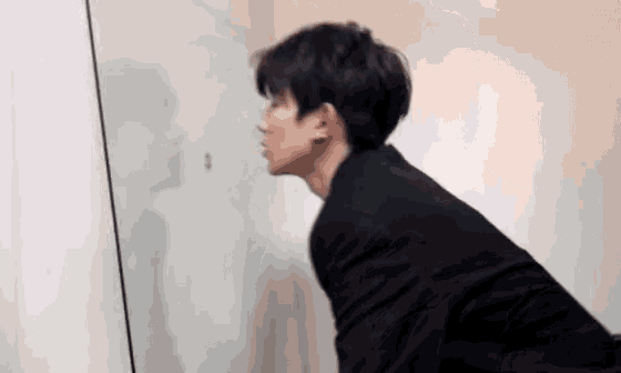 a man in a black suit is looking at his reflection in the mirror .