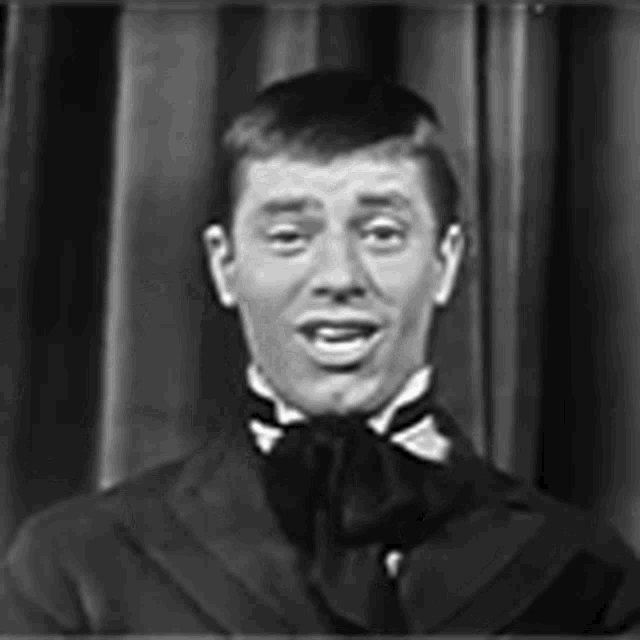 a black and white photo of a man in a tuxedo and bow tie making a funny face .
