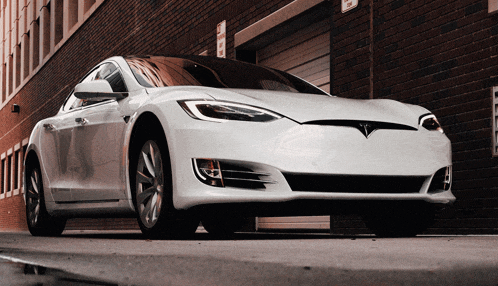 a white tesla model s is parked in front of a building