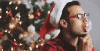 a man wearing a santa hat and glasses is licking a lollipop .