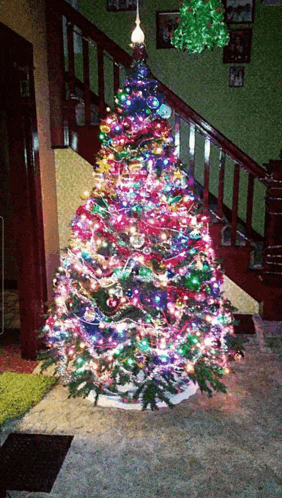 a christmas tree with a lot of lights on it in front of a staircase