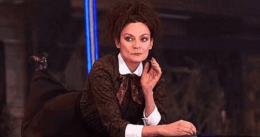 a woman in a brown dress is sitting at a table with her hand on her chin .