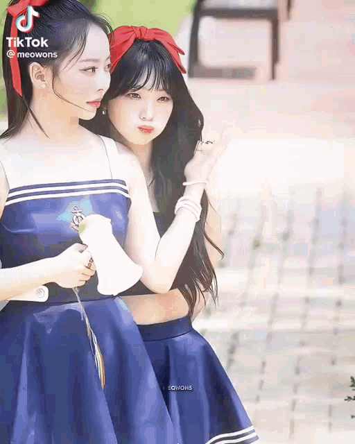 two girls in blue dresses are standing next to each other on a sidewalk .