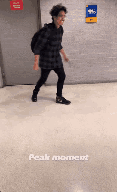 a man walking in a hallway with a sign that says peak moment on the floor