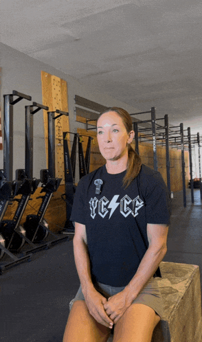 a woman wearing a black shirt that says peace sits on a box in a gym