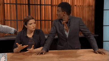 a man and a woman are sitting at a table with their hands on it