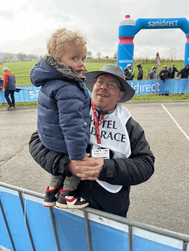 a man holding a child wearing a shirt that says hotel race on it