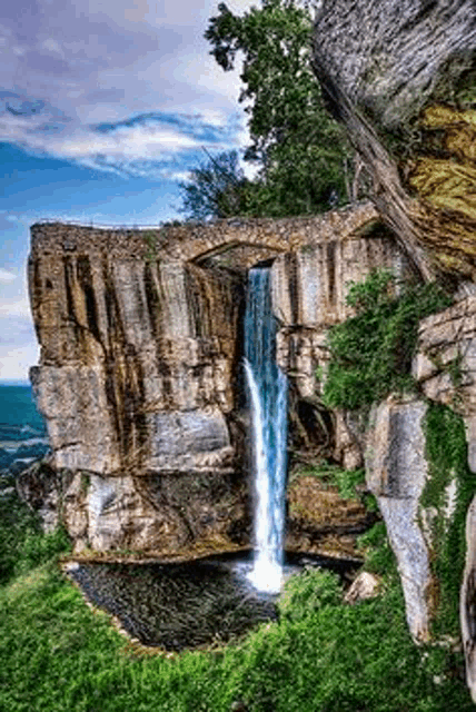 a waterfall is surrounded by rocks and trees on a cliff .