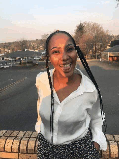 a woman wearing a white shirt and floral pants smiles in front of a parking lot