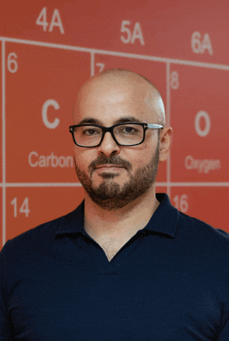 a man wearing glasses stands in front of a periodic table that says carbon