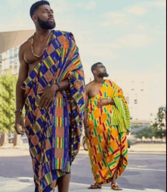 two men are standing next to each other on a sidewalk wearing traditional african clothing .