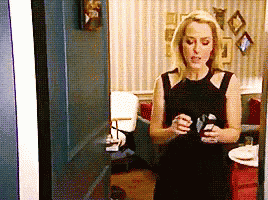 a woman in a black dress is standing in a room holding a cup