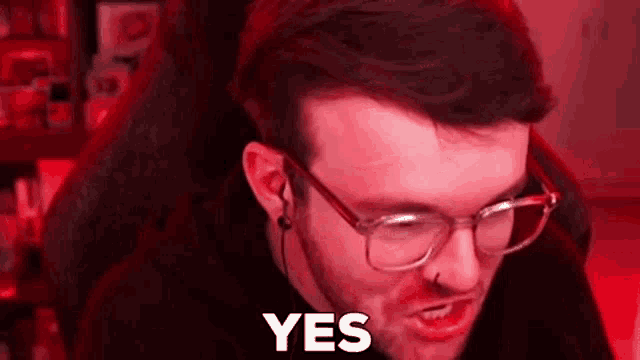 a man wearing glasses and ear buds is making a funny face while sitting in front of a computer .