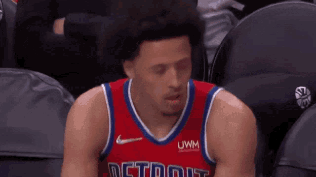 a basketball player is sitting in the stands during a game wearing a red jersey with the word detroit on it .