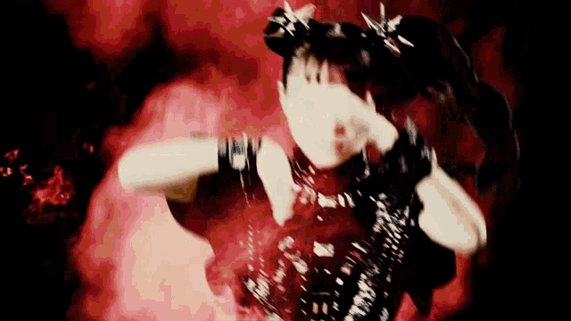 a woman in a black dress with spikes on her hair is dancing in front of a red background