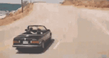 a convertible car is driving down a road near the ocean
