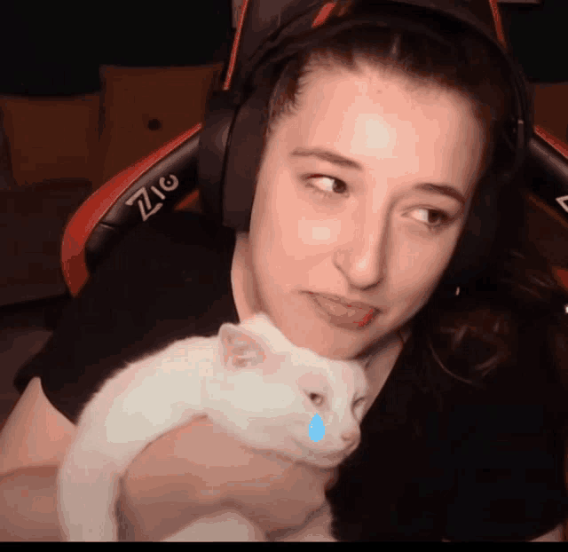 a woman wearing headphones is holding a white cat with a blue eye