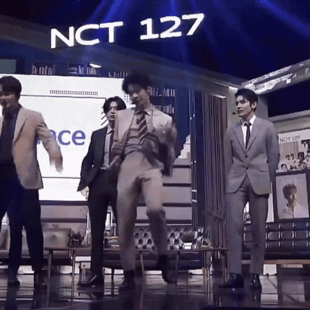 a group of men in suits are dancing in front of a nct 127 sign