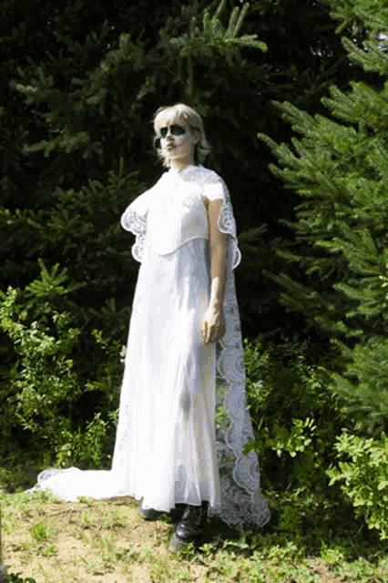 a woman in a white dress with a lace cape is standing in the woods