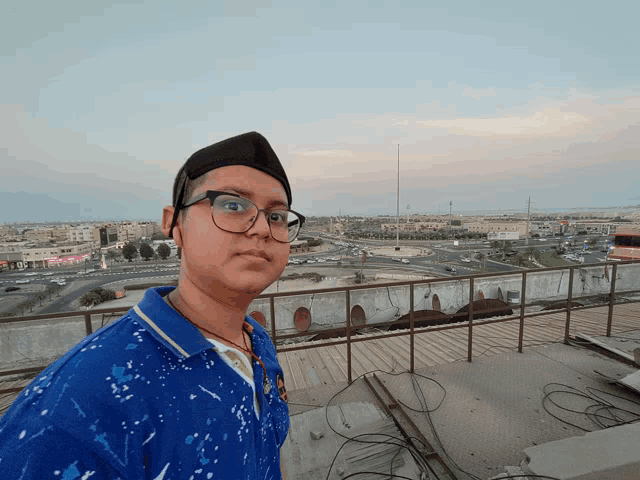 a boy wearing glasses and a blue shirt stands on a rooftop