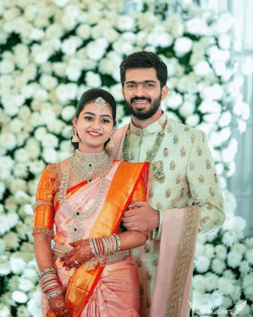 a bride and groom are posing for a picture in front of a wall of white flowers