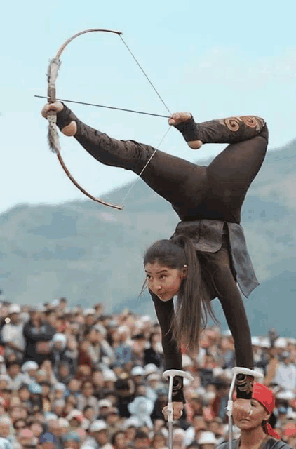 a woman with a bow and arrow is doing a handstand