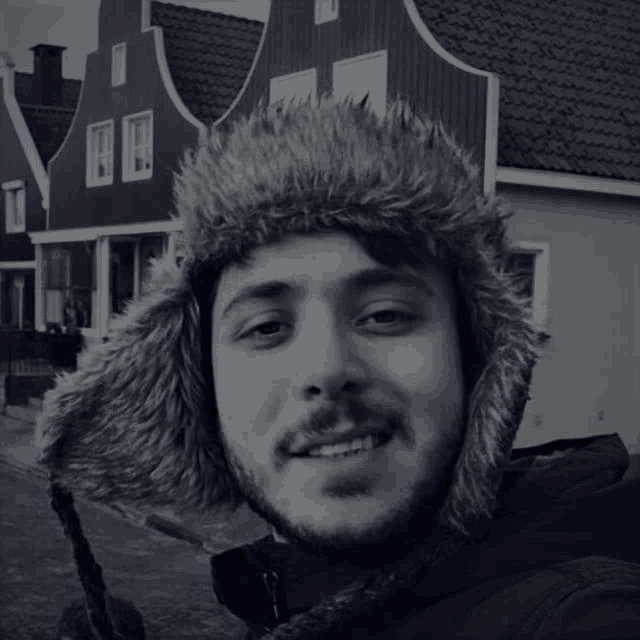 a man wearing a fur hat is smiling in front of a row of houses