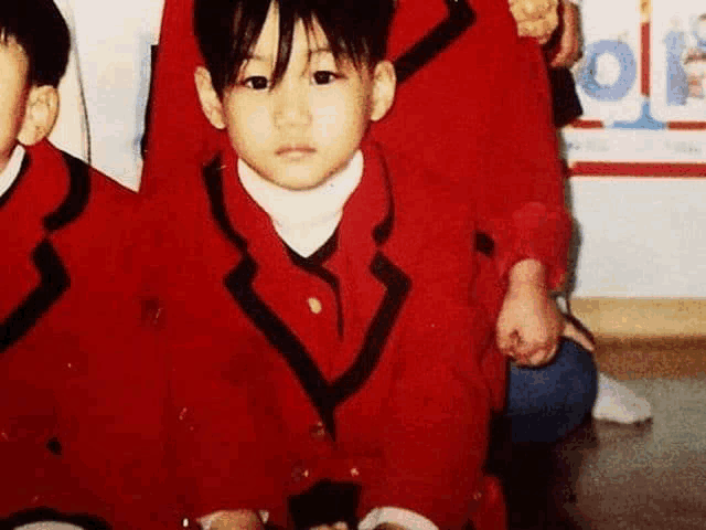 a young boy in a red jacket with black trim is sitting next to another child in a classroom .