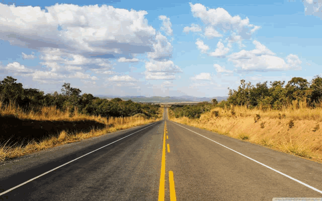 an empty road with a blue sky and clouds