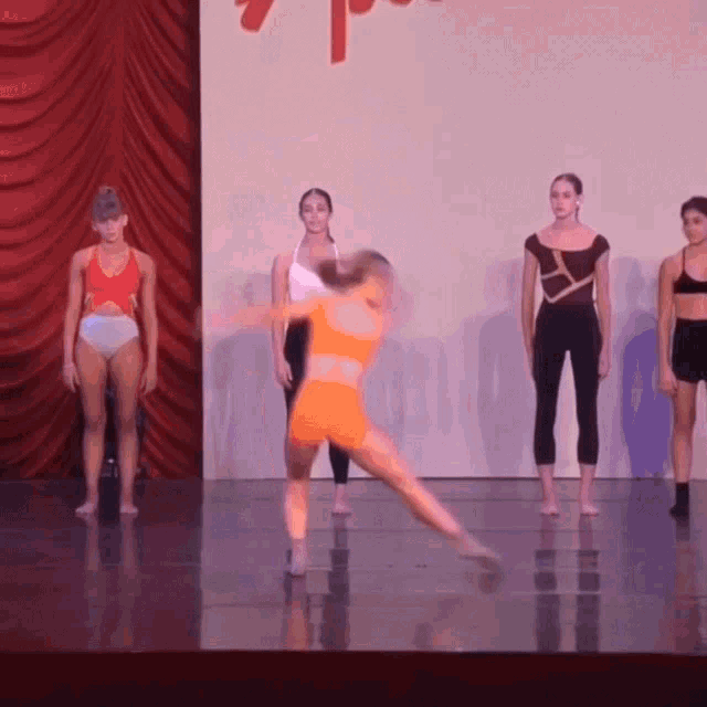 a group of young women are dancing on a stage with a red curtain behind them and a sign that says 7